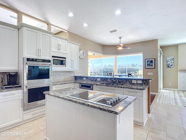 kitchen with sink, stainless steel appliances, a kitchen island, and white cabinetry