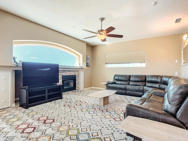 living room featuring ceiling fan and a stone fireplace