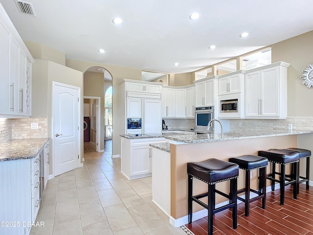 kitchen with a kitchen breakfast bar, kitchen peninsula, white cabinets, light stone counters, and built in appliances