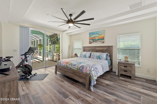 bedroom with access to outside, dark wood-type flooring, a textured ceiling, a raised ceiling, and ceiling fan