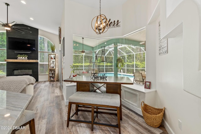 dining area with a large fireplace, vaulted ceiling, ceiling fan with notable chandelier, and wood-type flooring