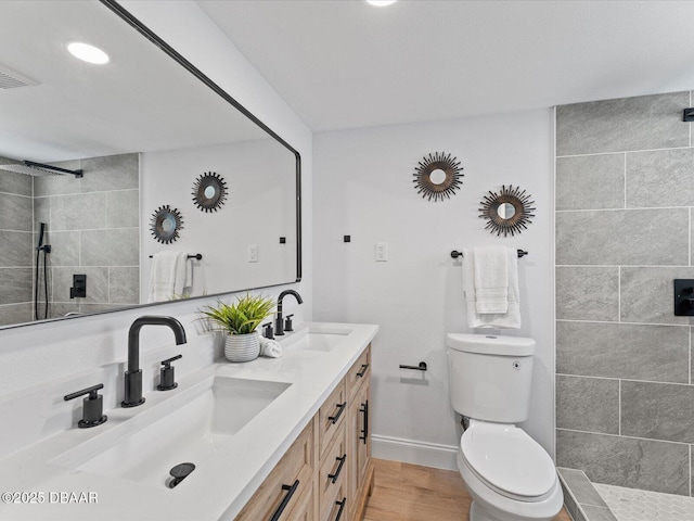 bathroom featuring a sink, a tile shower, toilet, and wood finished floors