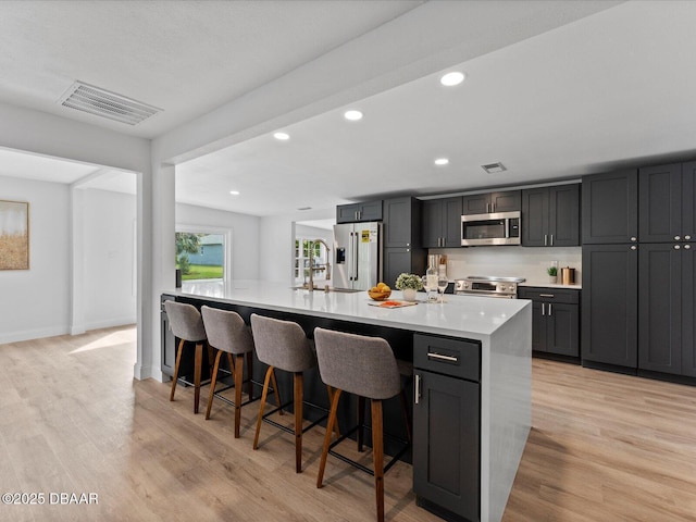 kitchen with a breakfast bar area, light countertops, light wood-style flooring, stainless steel appliances, and recessed lighting