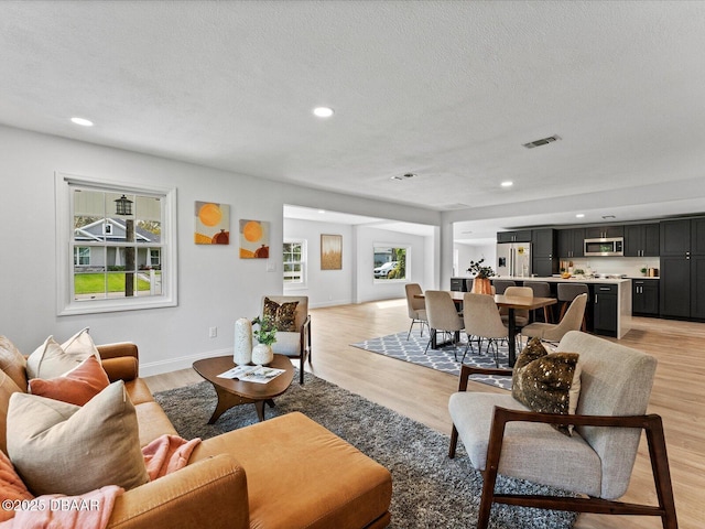 living area with a textured ceiling, light wood-style flooring, recessed lighting, indoor bar, and visible vents
