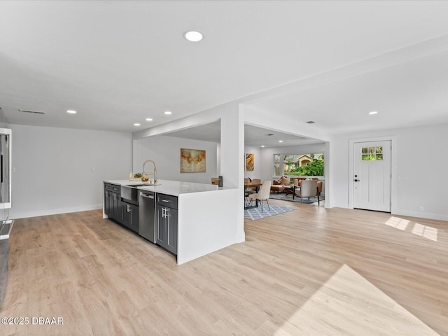 kitchen with stainless steel dishwasher, light countertops, a sink, open floor plan, and recessed lighting
