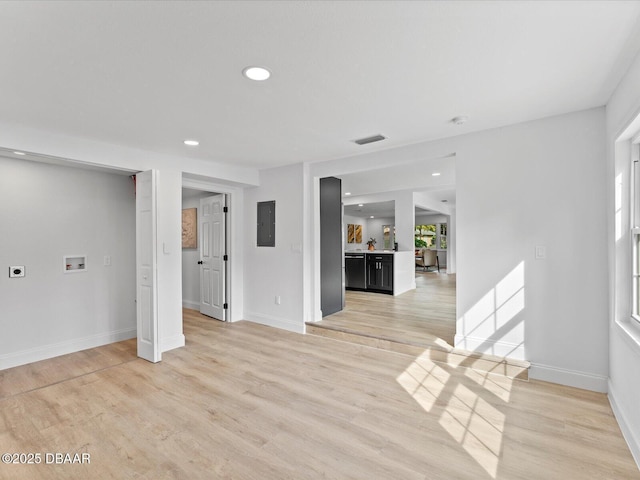 unfurnished living room with light wood finished floors, baseboards, electric panel, and recessed lighting