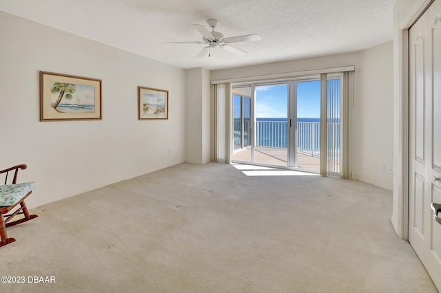 carpeted spare room with a water view, a textured ceiling, and ceiling fan