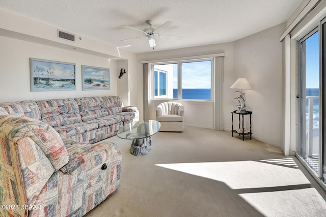 living room featuring a textured ceiling, a water view, light carpet, and ceiling fan