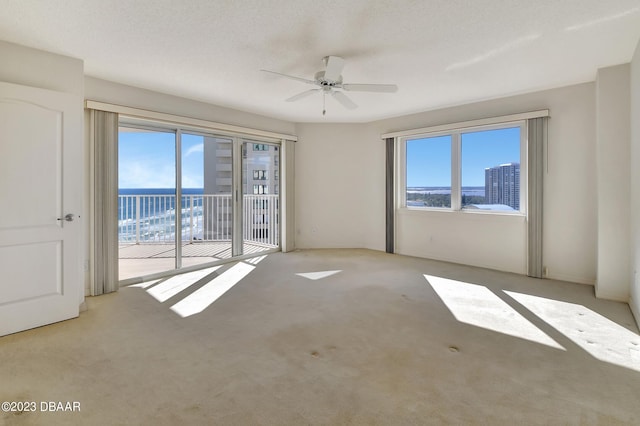 carpeted spare room with a textured ceiling, plenty of natural light, a water view, and ceiling fan