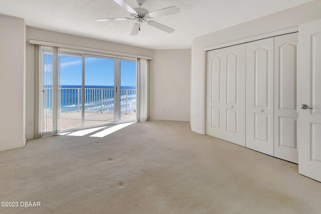 unfurnished bedroom featuring a closet, a water view, light colored carpet, and access to exterior