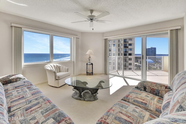 living room featuring carpet floors, a water view, a textured ceiling, and ceiling fan