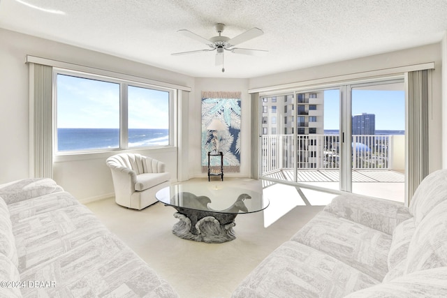 living room featuring ceiling fan, a textured ceiling, a water view, and carpet floors