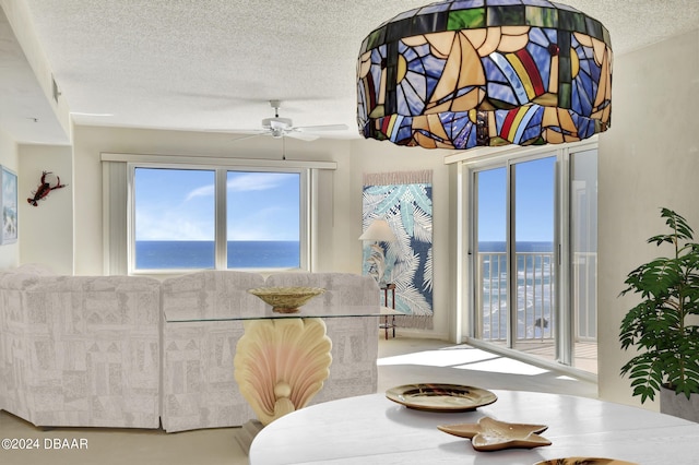 dining area with ceiling fan, a textured ceiling, and a water view