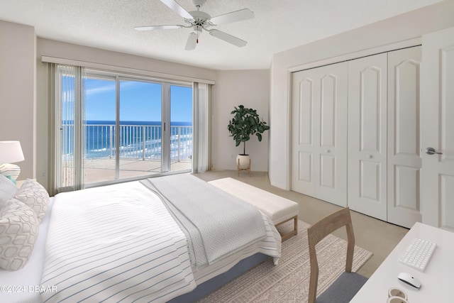 bedroom with a water view, access to exterior, a textured ceiling, ceiling fan, and a closet