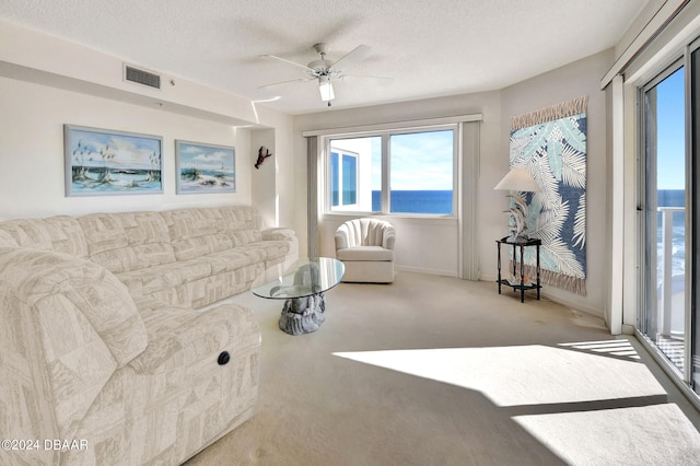 carpeted living room featuring a water view, a textured ceiling, and ceiling fan