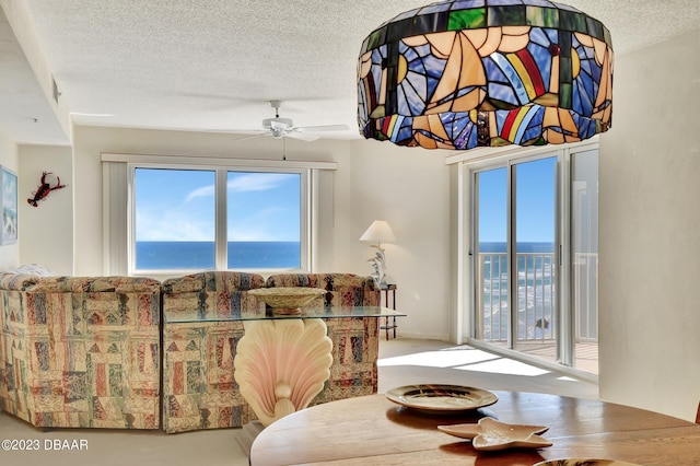 living room with a water view, a textured ceiling, and ceiling fan