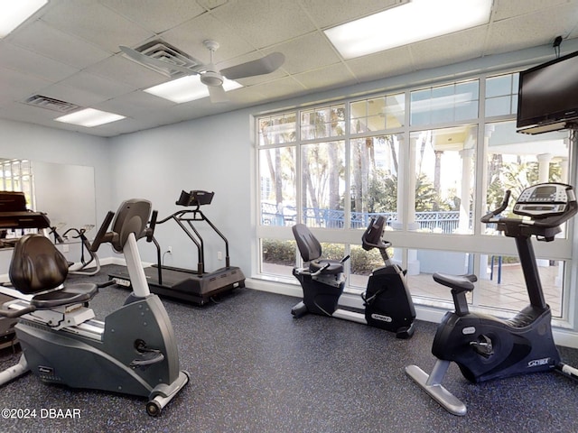 gym featuring a paneled ceiling, ceiling fan, and a healthy amount of sunlight