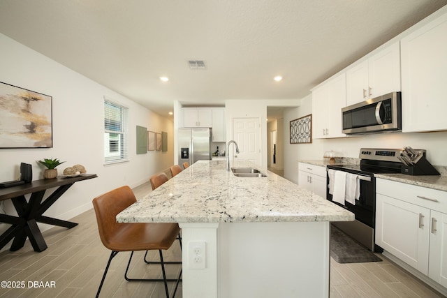 kitchen with visible vents, a breakfast bar, wood tiled floor, stainless steel appliances, and a sink