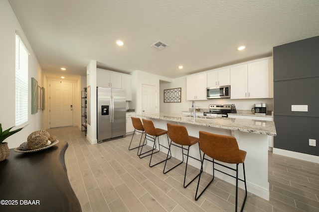 kitchen with appliances with stainless steel finishes, a breakfast bar area, light wood-type flooring, and white cabinets