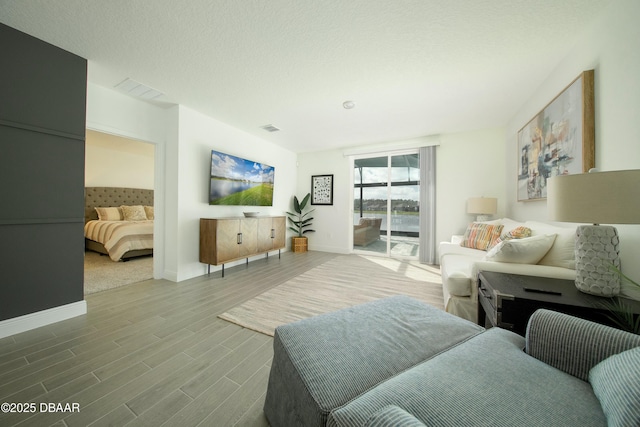 living room featuring a textured ceiling, wood finished floors, visible vents, and baseboards