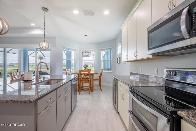 kitchen featuring pendant lighting, a center island with sink, sink, white cabinetry, and stainless steel appliances