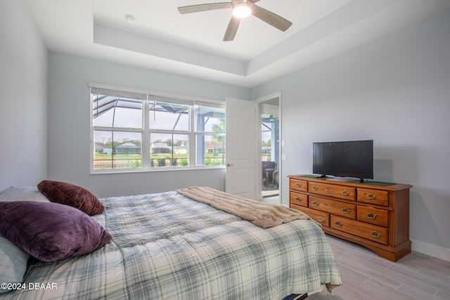 bedroom featuring ceiling fan, light hardwood / wood-style flooring, and a tray ceiling