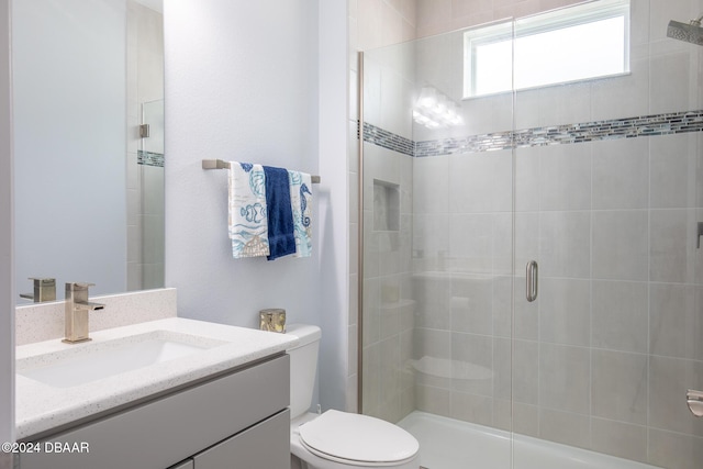 bathroom featuring a shower with shower door, toilet, and vanity