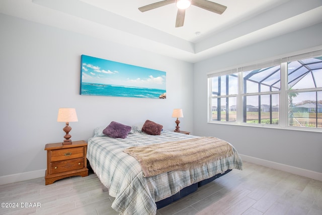 bedroom with ceiling fan, light hardwood / wood-style flooring, multiple windows, and a raised ceiling