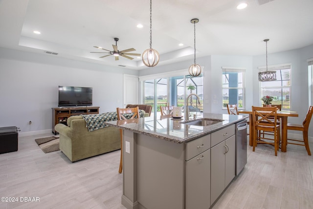 kitchen with a raised ceiling, sink, light hardwood / wood-style floors, and a center island with sink