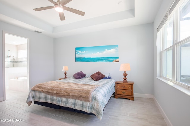 bedroom featuring ceiling fan, ensuite bathroom, and a raised ceiling