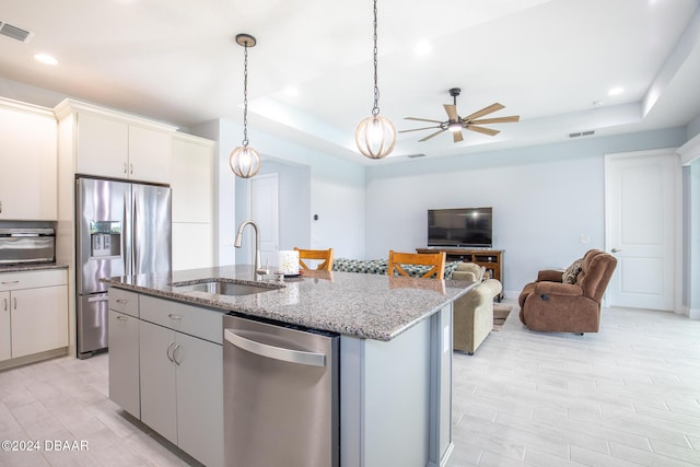 kitchen with white cabinetry, stainless steel appliances, sink, a raised ceiling, and a center island with sink