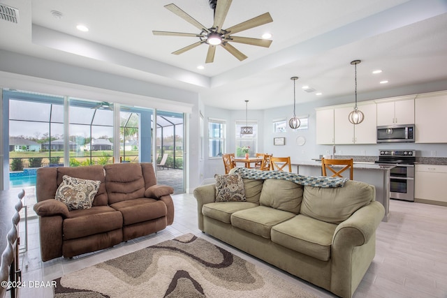 living room featuring ceiling fan, a tray ceiling, and light hardwood / wood-style flooring