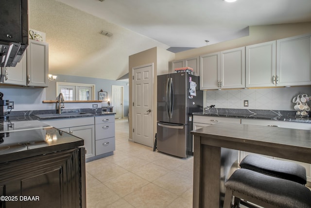 kitchen with gray cabinets, vaulted ceiling, light tile patterned flooring, stainless steel refrigerator, and sink