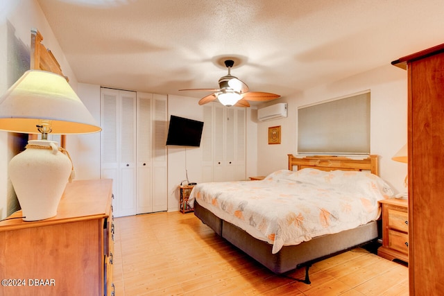 bedroom featuring a textured ceiling, ceiling fan, light hardwood / wood-style flooring, and a wall mounted air conditioner