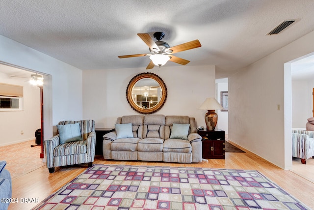 living room featuring ceiling fan, light hardwood / wood-style floors, and a textured ceiling