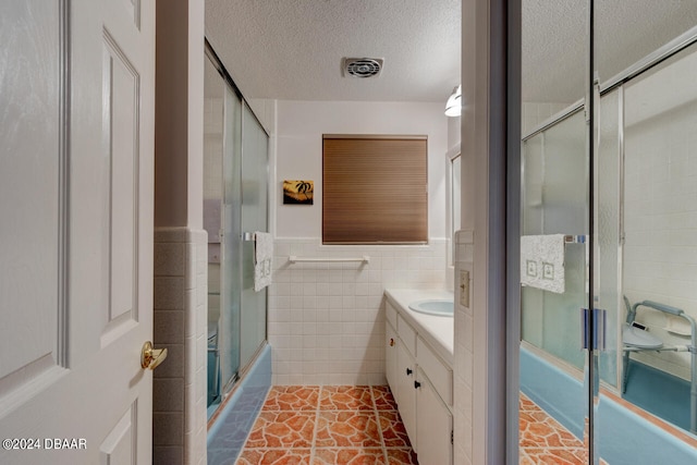 bathroom with tile patterned flooring, enclosed tub / shower combo, a textured ceiling, vanity, and tile walls