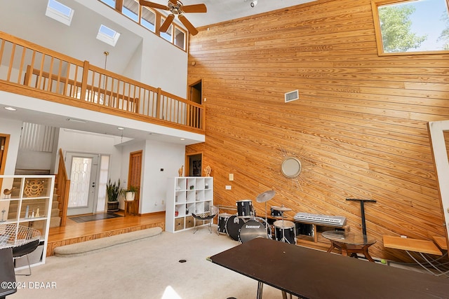 living room with carpet, a towering ceiling, wood walls, a skylight, and ceiling fan