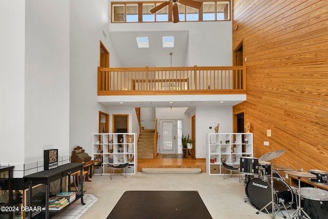 living room featuring wood walls, a high ceiling, ceiling fan, and plenty of natural light