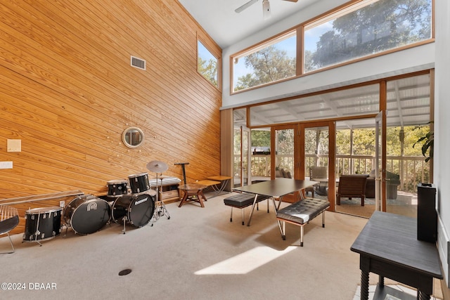 carpeted living room featuring high vaulted ceiling, wooden walls, and ceiling fan