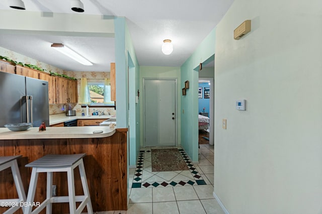 kitchen featuring a breakfast bar, stainless steel fridge, kitchen peninsula, and light tile patterned floors