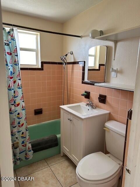 bathroom with tile walls, toilet, tile patterned floors, shower / bath combination with curtain, and vanity