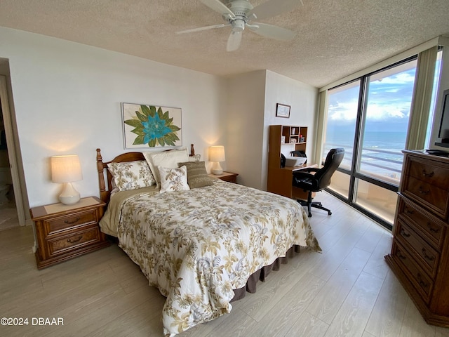 bedroom with ceiling fan, a wall of windows, a textured ceiling, access to exterior, and light hardwood / wood-style flooring