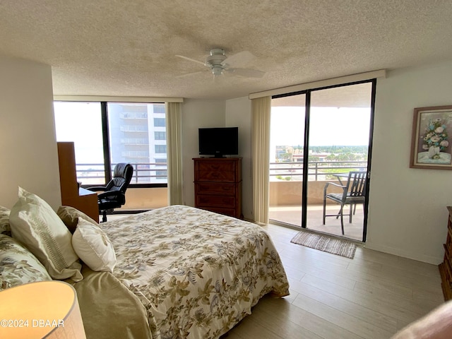 bedroom featuring expansive windows, light hardwood / wood-style floors, access to exterior, and a textured ceiling