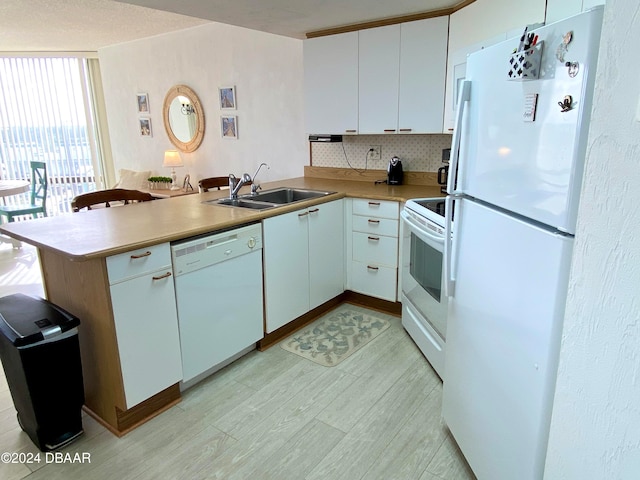 kitchen with white cabinets, kitchen peninsula, sink, tasteful backsplash, and white appliances