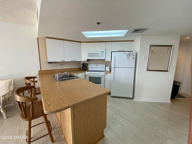 kitchen with kitchen peninsula, sink, white cabinetry, light wood-type flooring, and white appliances