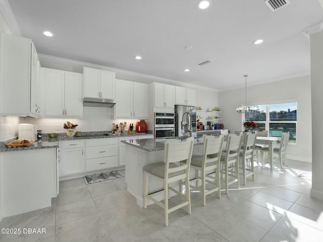 kitchen featuring a center island with sink, ornamental molding, dark stone countertops, and white cabinets