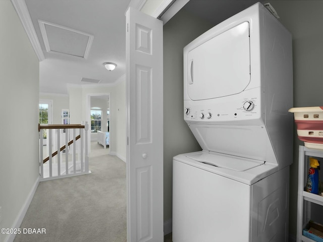 clothes washing area with crown molding, light colored carpet, and stacked washer / drying machine