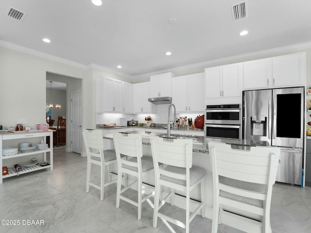 kitchen with appliances with stainless steel finishes, a kitchen bar, a kitchen island with sink, and white cabinets