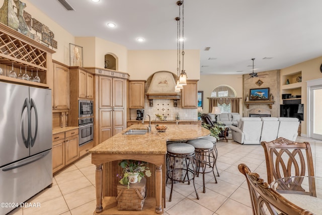 kitchen featuring stainless steel appliances, sink, an island with sink, pendant lighting, and a large fireplace