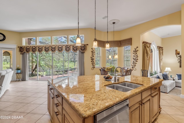 kitchen with a center island with sink, sink, stainless steel dishwasher, light stone countertops, and pendant lighting